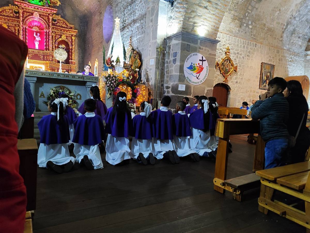 Ministrantes arrodillados frente al pesebre navideño